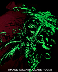 A RED garment featuring a glowing neon green gothic graphic of a skull, ornate scrollwork, and a large cross, shown against a dark background with a red fabric element. Text at the bottom reads '(IMAGE TAKEN IN A DARK ROOM)'.