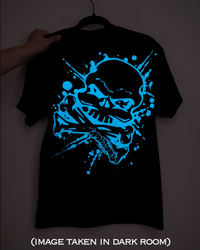 A black short-sleeve T-shirt hanging on a hanger, with a large glowing blue skull and crossbones graphic on the front. A hand is holding the left shoulder area, and the photo is taken in a dark room.
